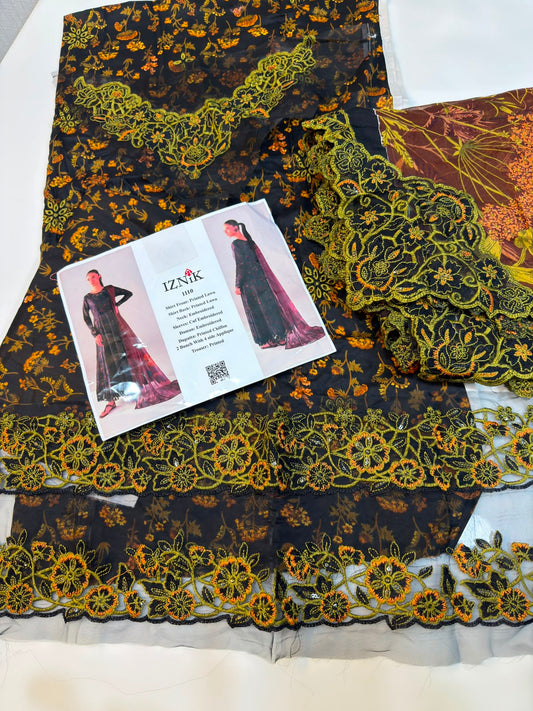A folded black fabric outfit set with yellow and orange floral embroidery and lace trim, displayed on a white surface with a printed brand card